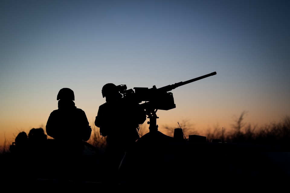 Silhouette of Ukrainian soldiers operating an anti-aircraft gun at sunset.